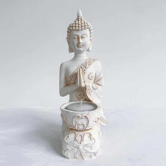 Front view of buddha kneeling, candle holder on lap, with ornate robes and detailing, natural off white colors.