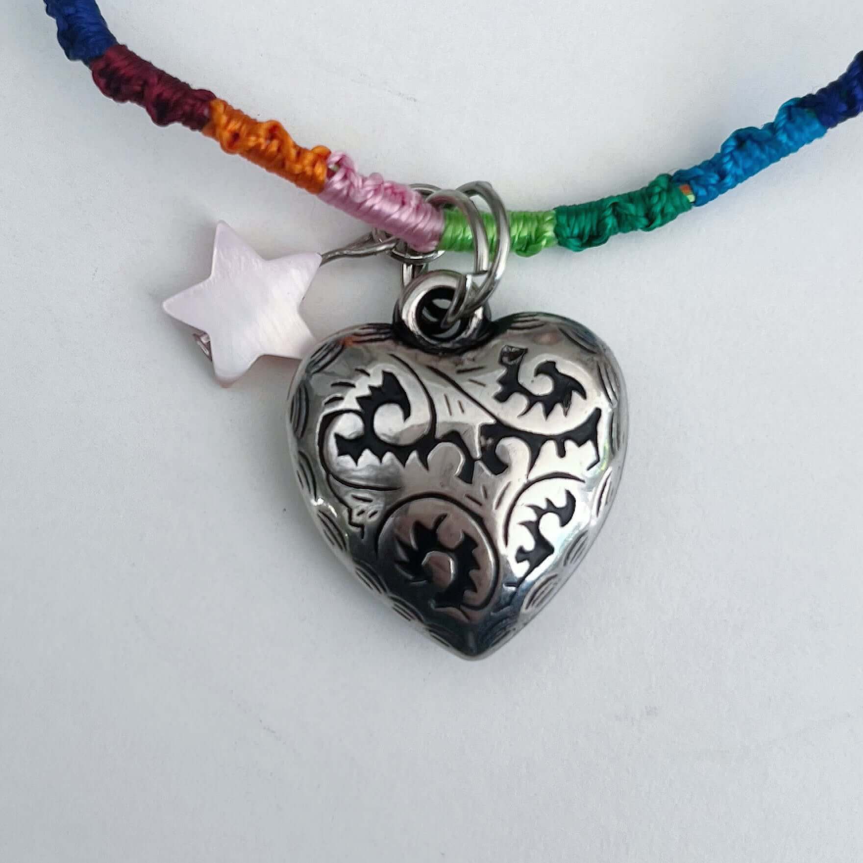 Detail of silver metal filigree heart 25mm, little mother of pearl star, on silky multi colored, wound and knotted thread.