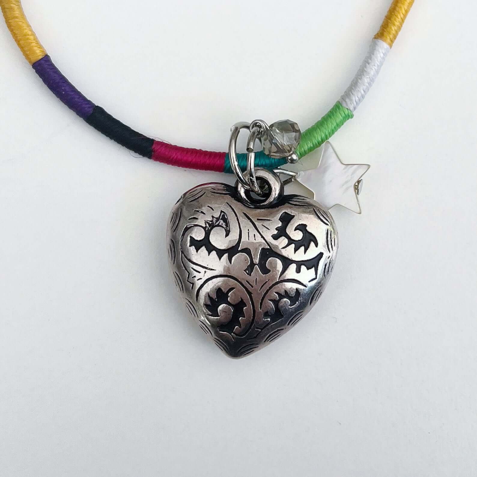 Detail of silver metal filigree heart 25mm, little mother of pearl star, on silky multi colored, wound and knotted thread.