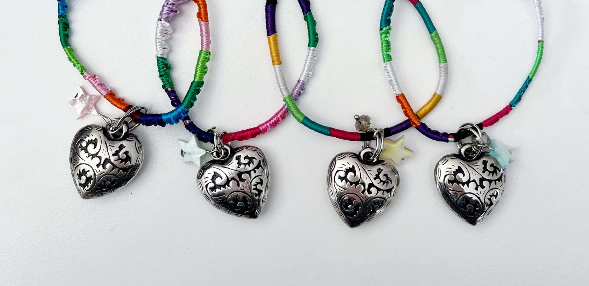 Group of 4 different silver metal filigree heart 25mm, little mother of pearl star, on silky multi colored thread.