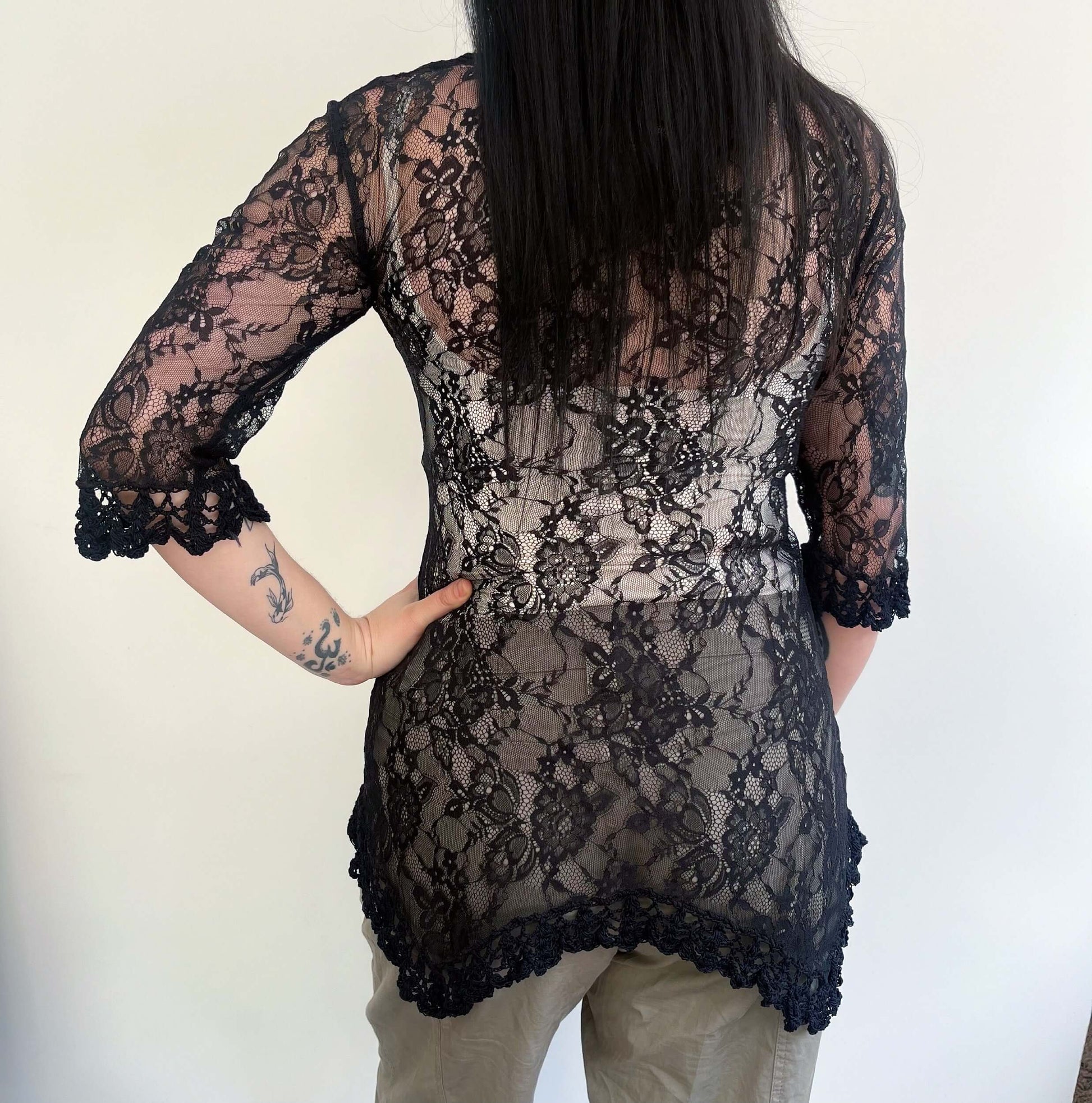 Back view of black lace three quarter sleeve tunic, with black crochet on the jagged hem, and edge of sleeve. 