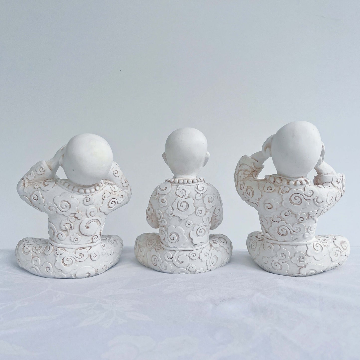 Back view of monks in a row, all natural off white colors, with ornate robes.