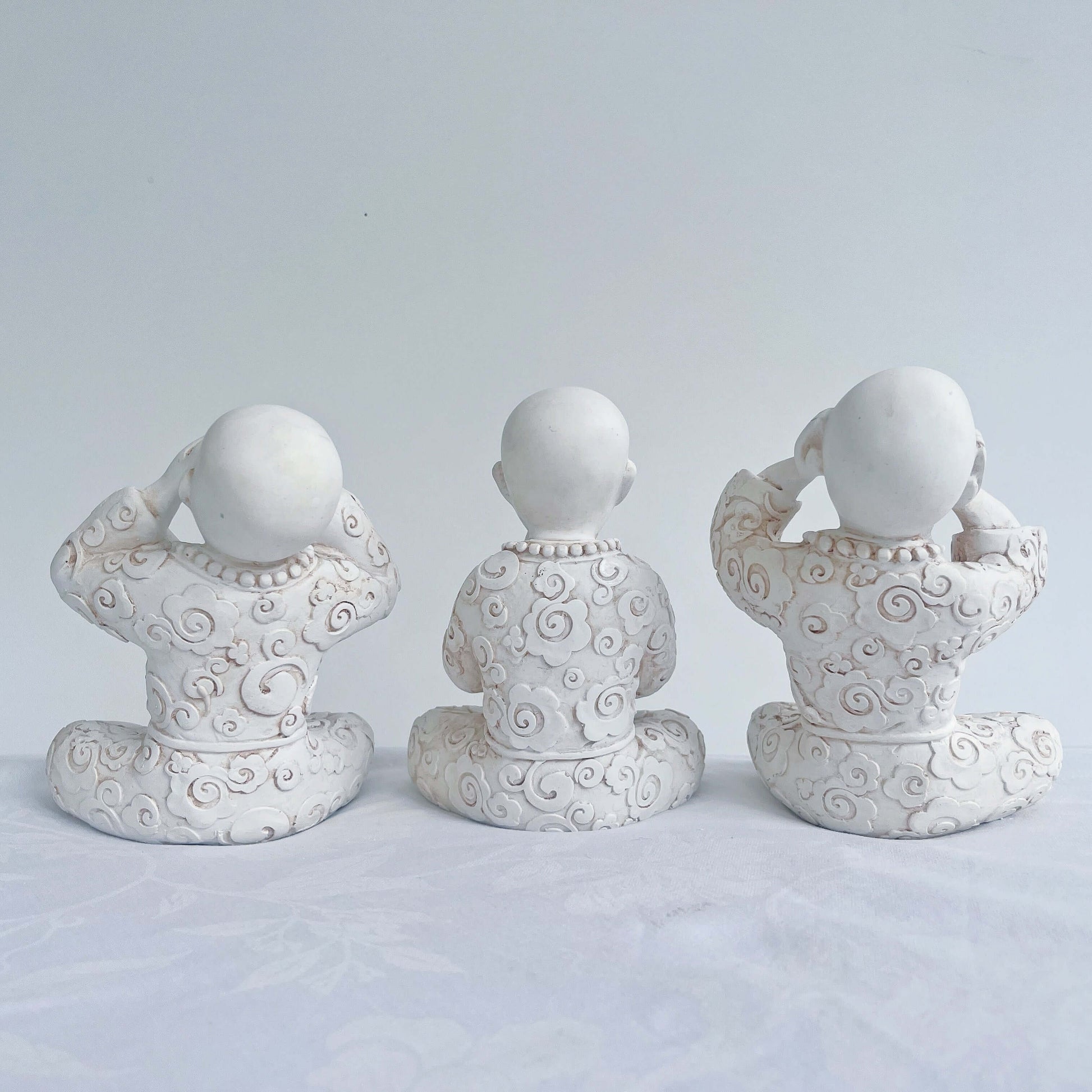Back view of monks in a row, all natural off white colors, with ornate robes.