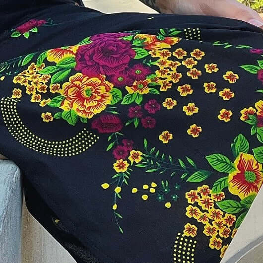 Fabric detail of the bright colorful bold floral hem border, with yellows, greens, and pink flowers on black.