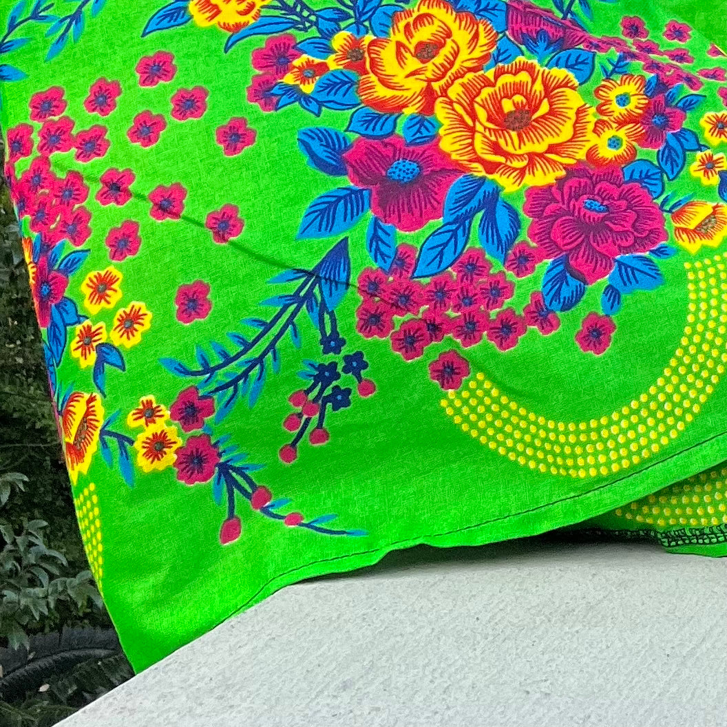 Fabric detail of the bright colorful bold floral hem border, with yellow, turquoise, and pink flowers on green background.