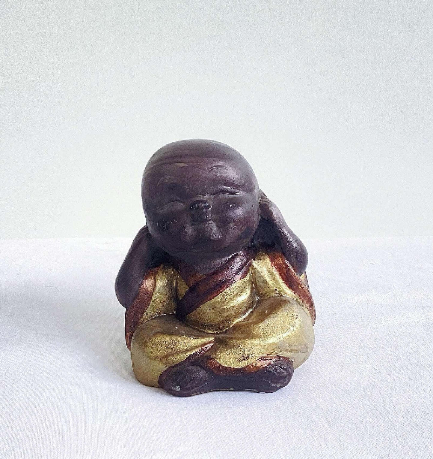 View of single monk, hear no evil, painted brown figure, with golden robes, and hands covering the ears.