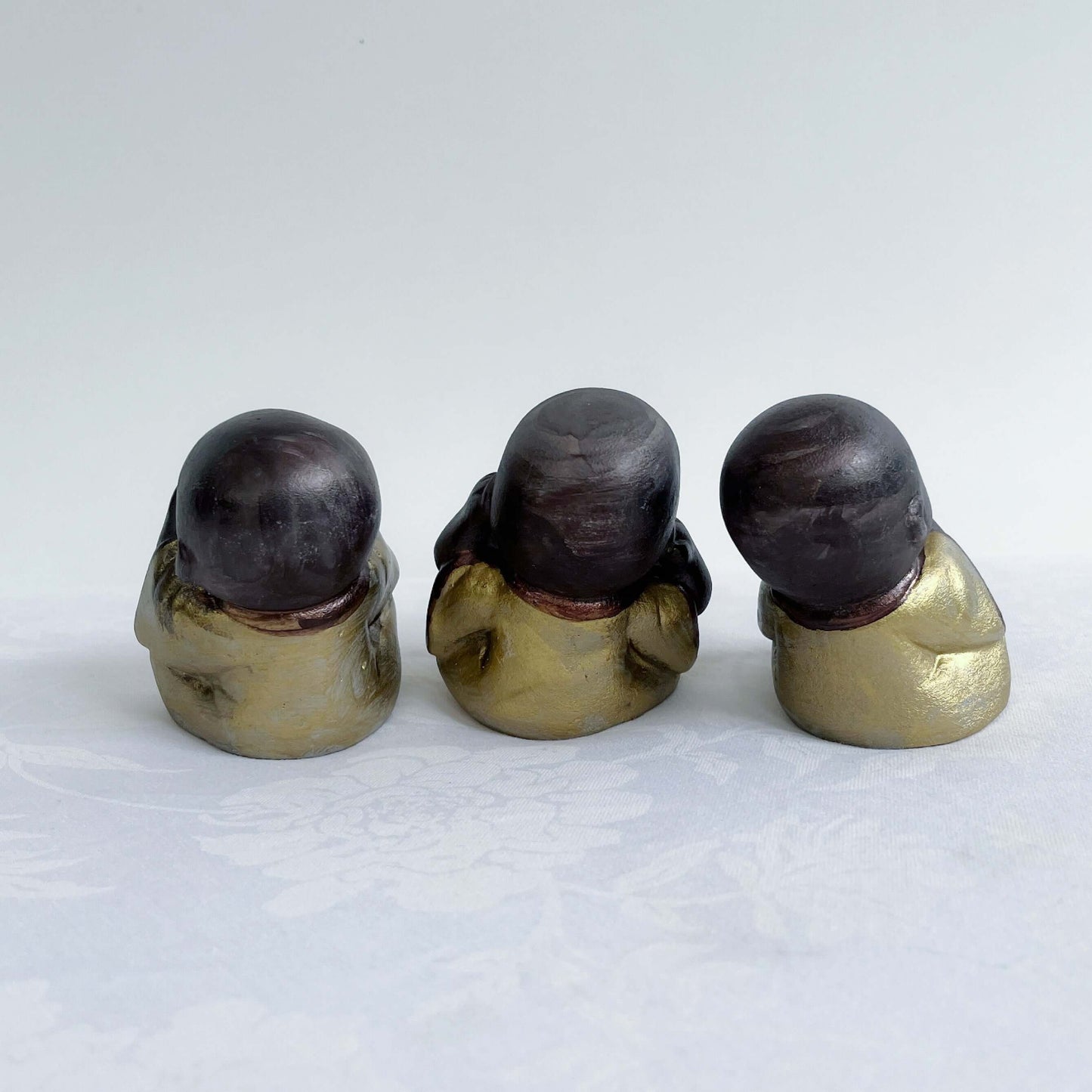 Back view of monks, all three in a row, brown painted figures with golden robes.