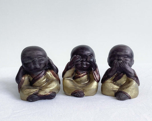 Front view of monks, all three in a row, brown painted figures with golden robes.
