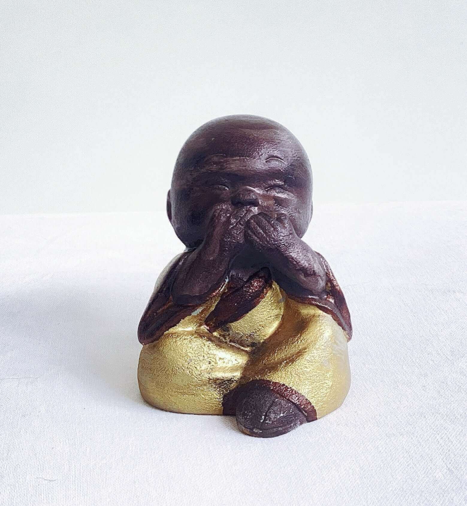 View of single monk, see no evil, painted brown figure, with golden robes, and hands covering the eyes.