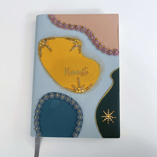 Top view of journal showing blotch of color in yellow, peach, blue, black, with crystal decorations on the borders.