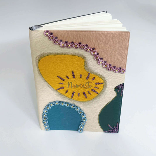 View of journal upright, showing blotches of color in yellow, peach, blue, black, with crystal deco on their borders.