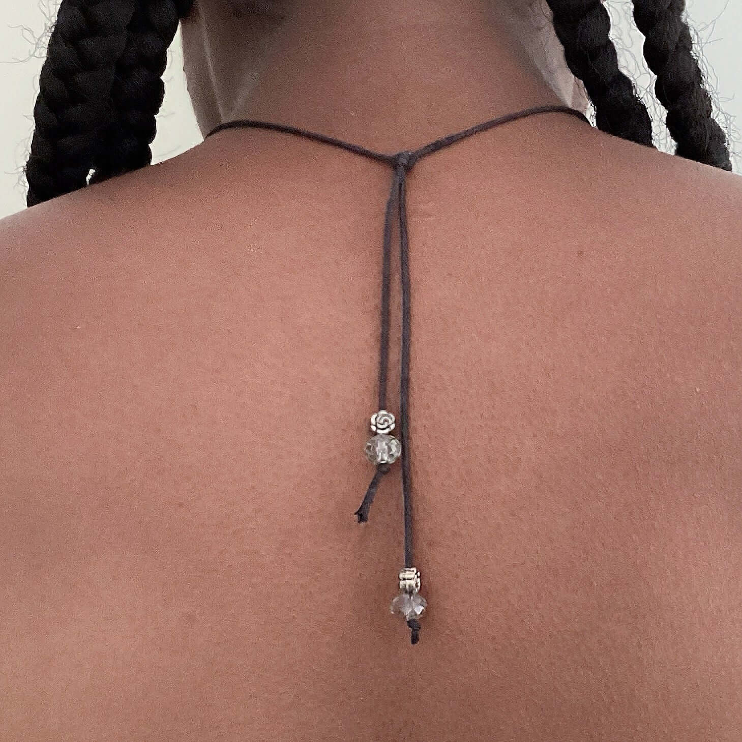 View of large metal om sign tied behind the neck on thin faux leather twine, adjustable length, beads on the ends.