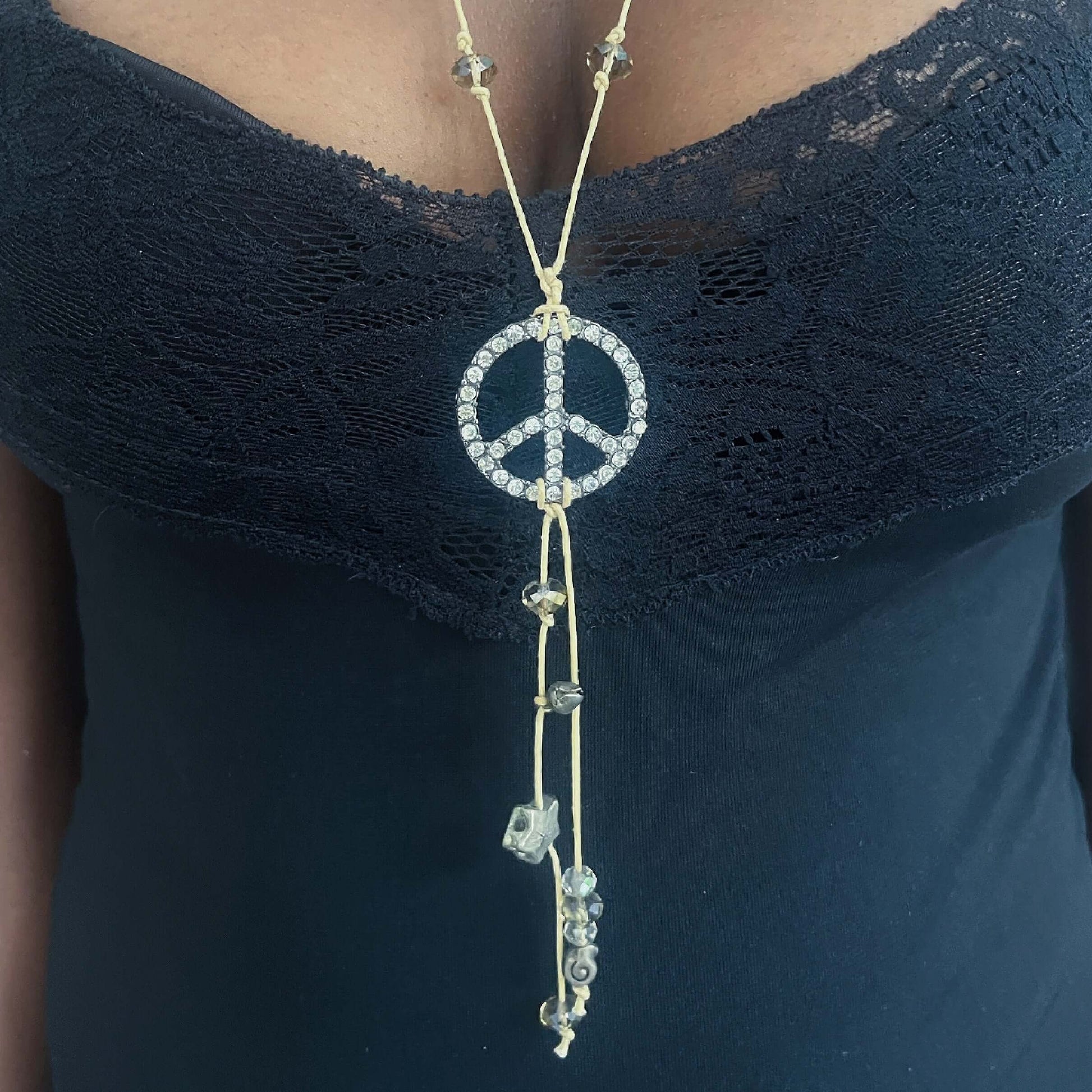 Detail view of beige thong necklace with diamante encrusted peace sign, with shorter thongs dangling from the center.