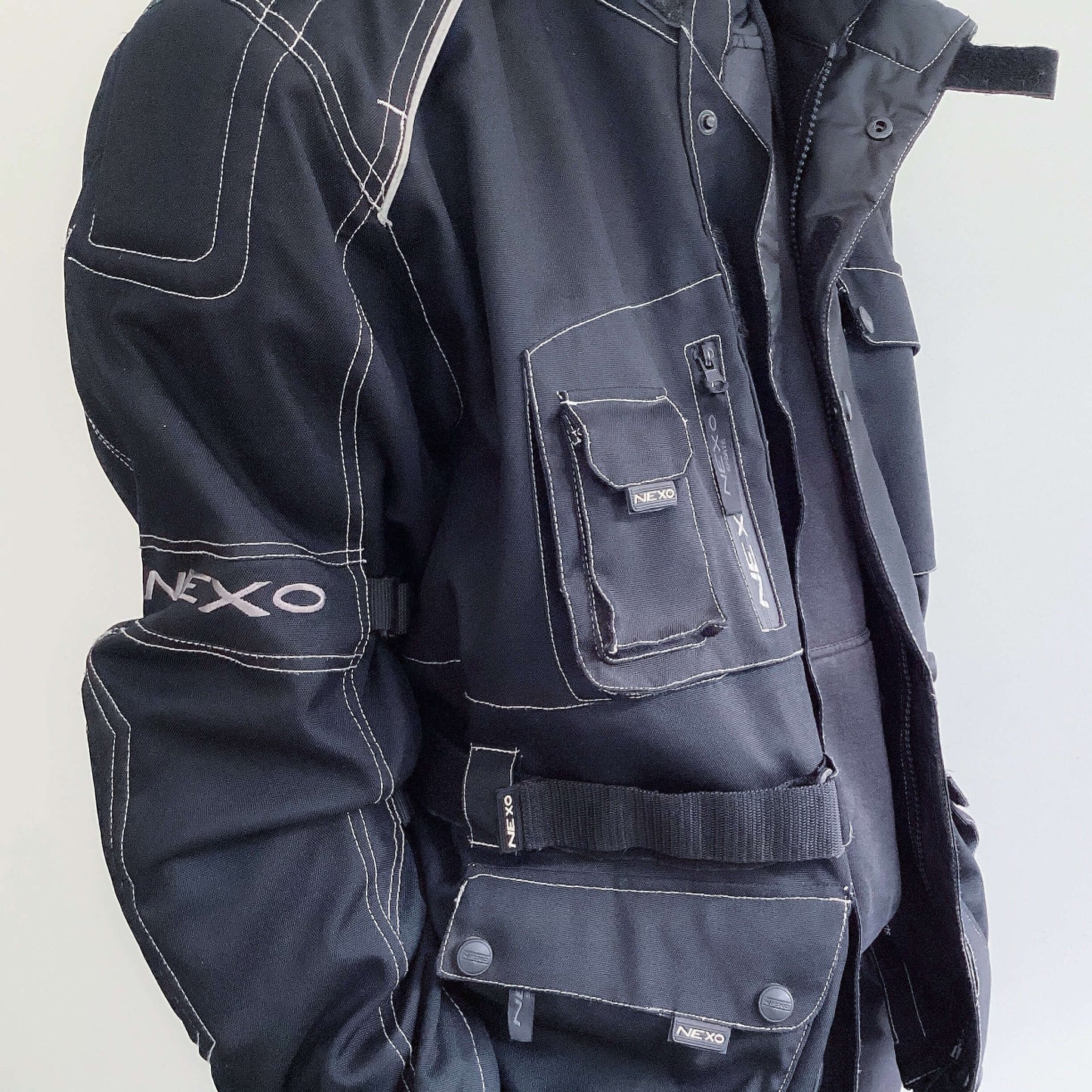 Detail view of well padded zipper jacket, black all over with white stitching on all edges, hip length, multiple pockets.