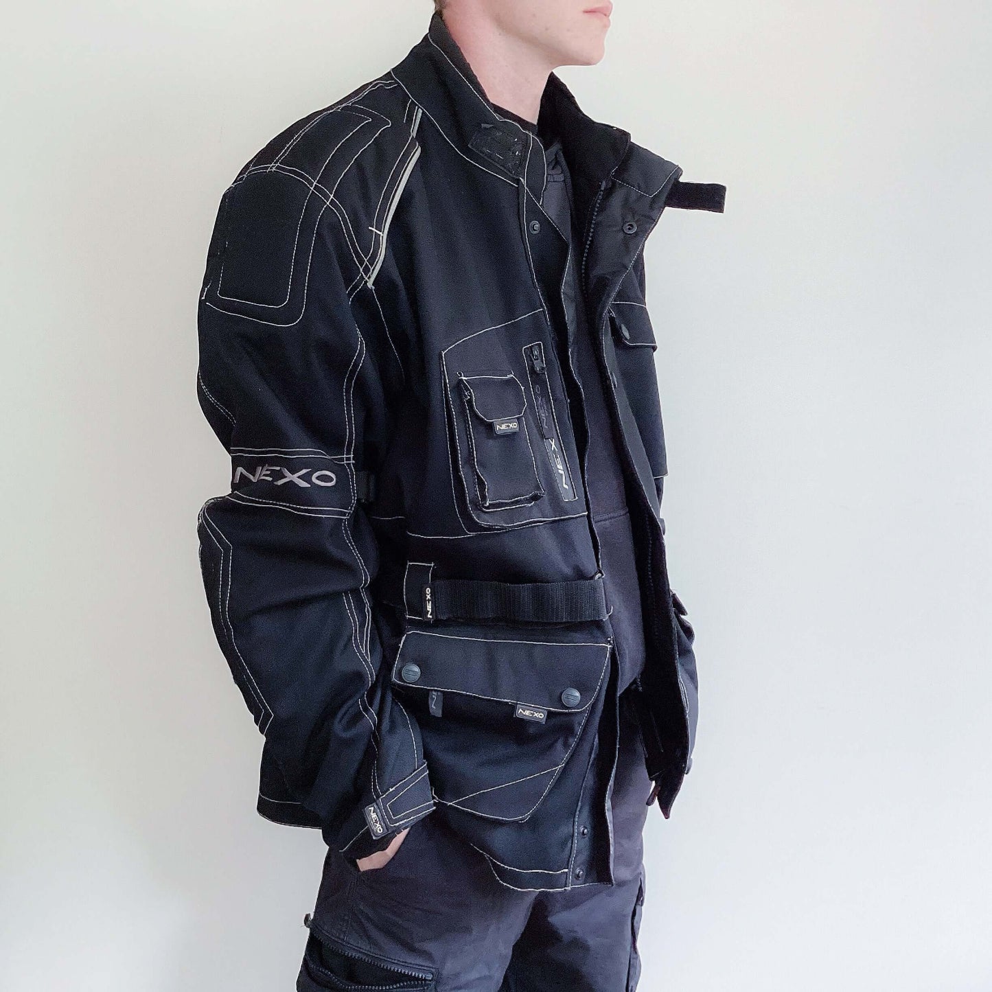 Side view of well padded zipper jacket, black all over with white stitching on all edges, hip length, multiple pockets.