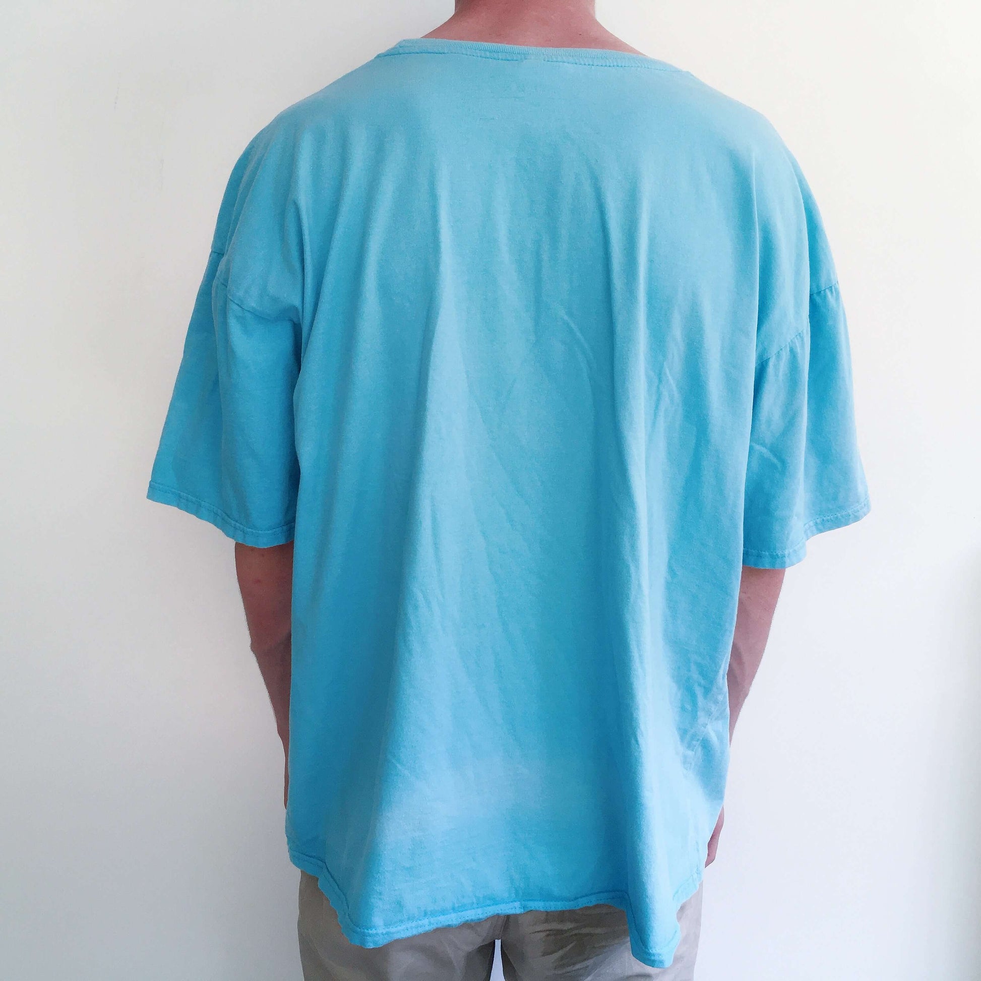 Back view of turquoise, drop shoulder tshirt, with black printing on the front.