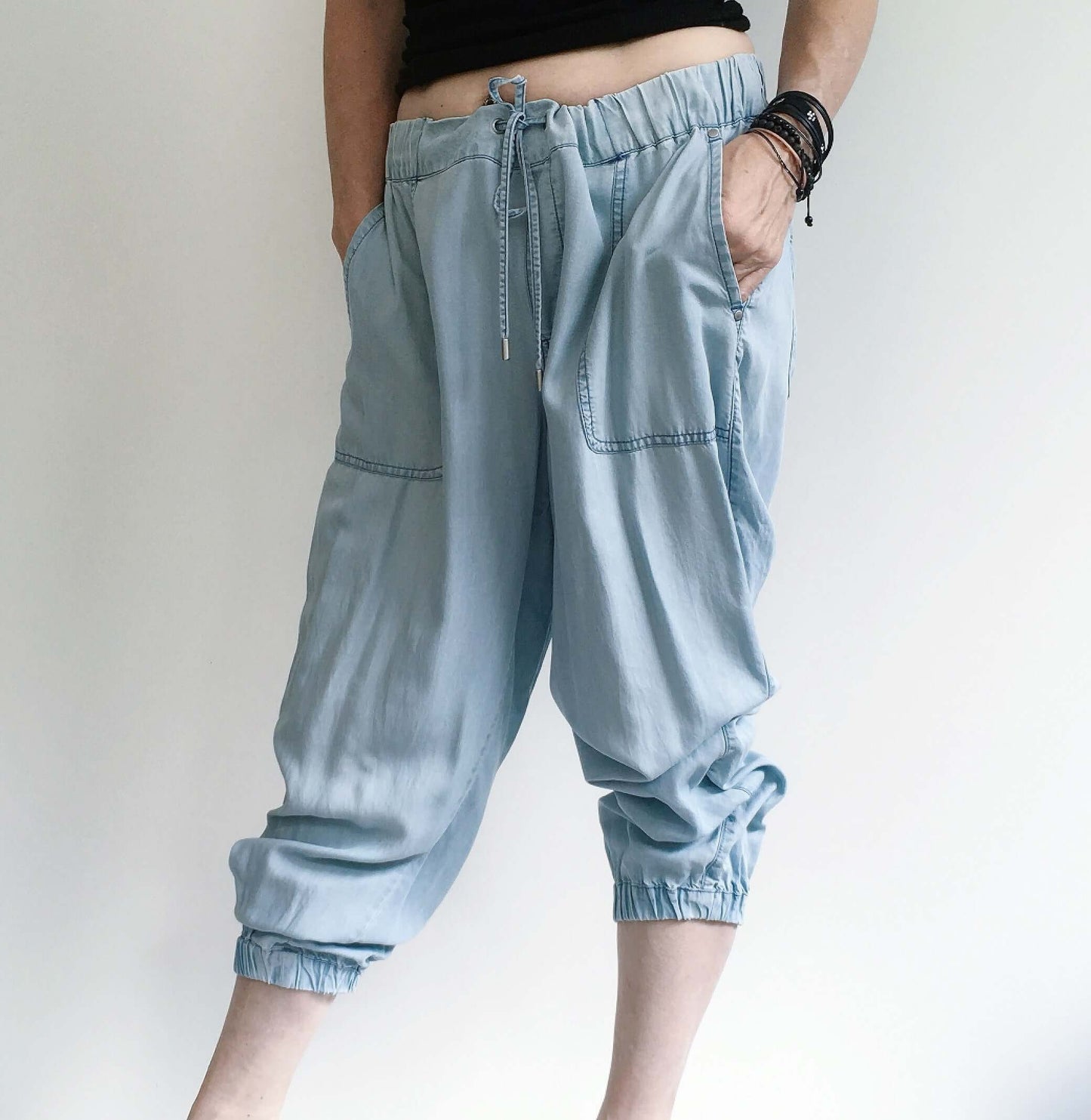 Front view of pale blue elasticated pants with drawstring, deep side pockets, and elasticated ankles pulled up to calf.