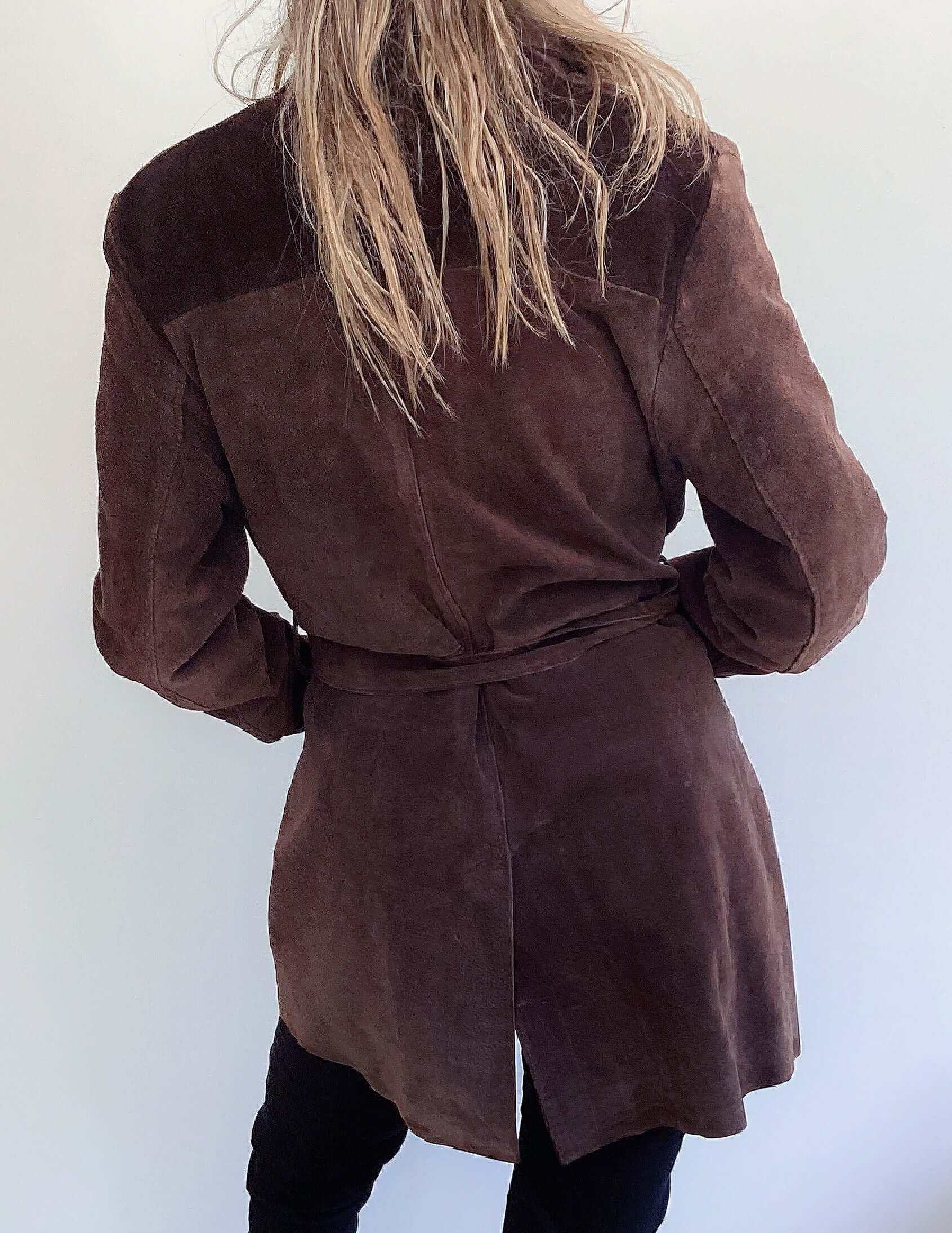 Back view of chocolate brown button up suede jacket, mid thigh length, with belt and pockets.