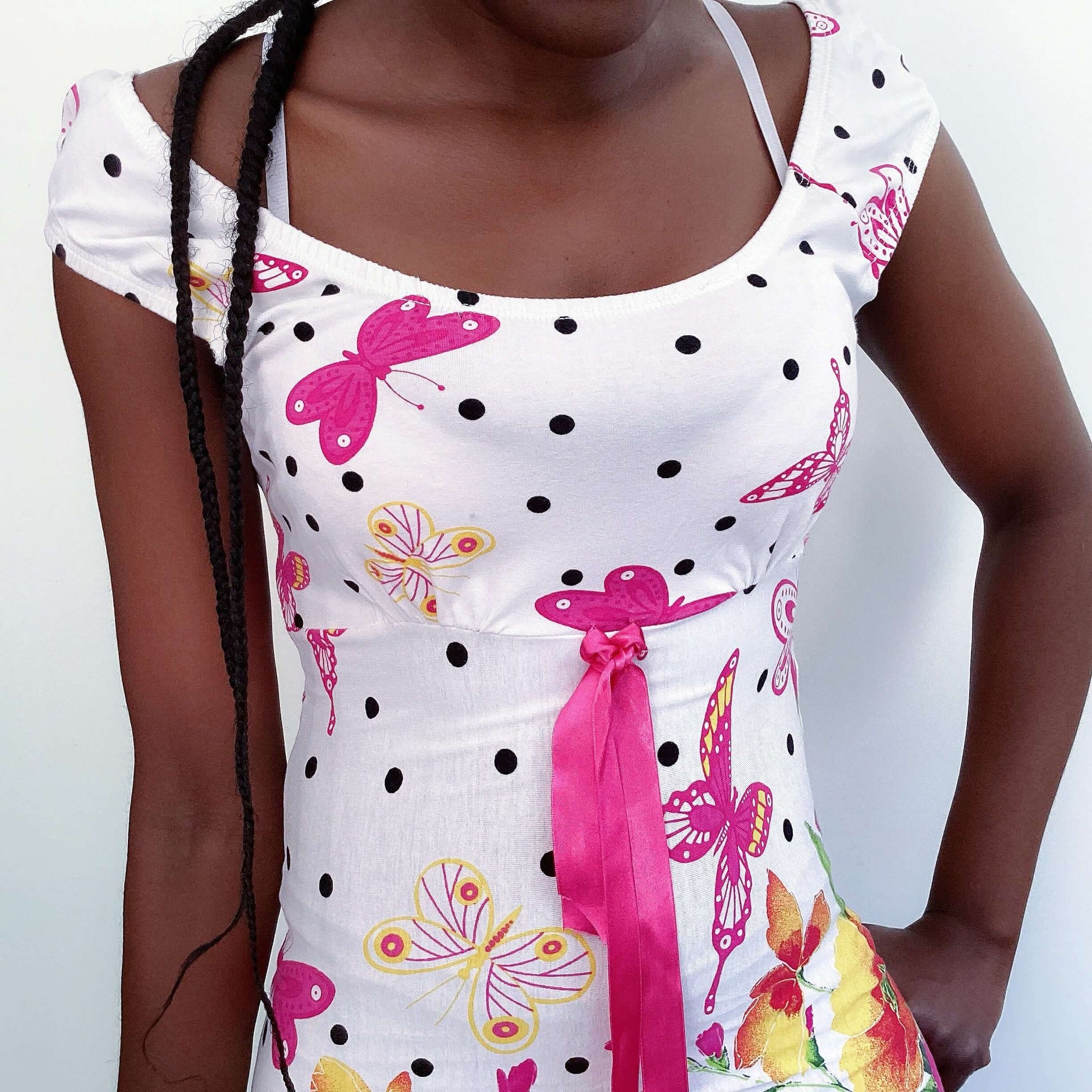 Detail view of white cotton mini dress with pink butterflies and roses, pink ribbon in the center under bust, and black dots.