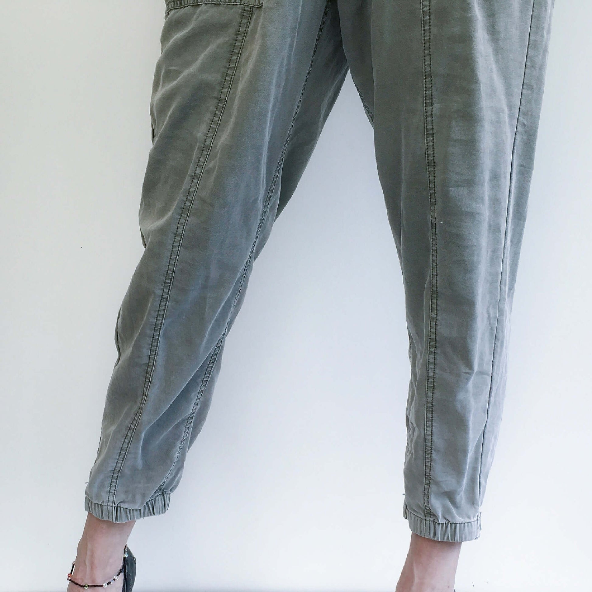 Detail view of pale khaki elasticated pants with belt, side pockets, and elasticated ankles.