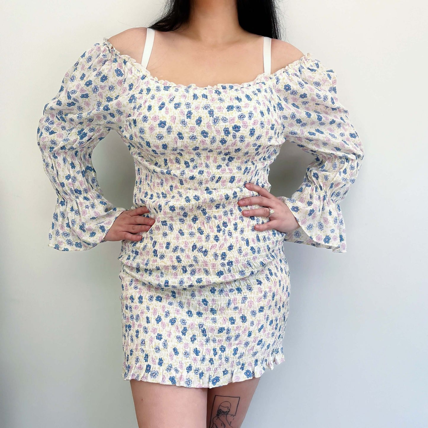 Front view printed cotton dress, elasticated off shoulder, ruched sleeve cuffs, bodice, and hips. Model has hands on hips