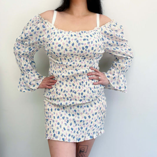 Front view printed cotton dress, elasticated off shoulder, ruched sleeve cuffs, bodice, and hips. Model has hands on hips