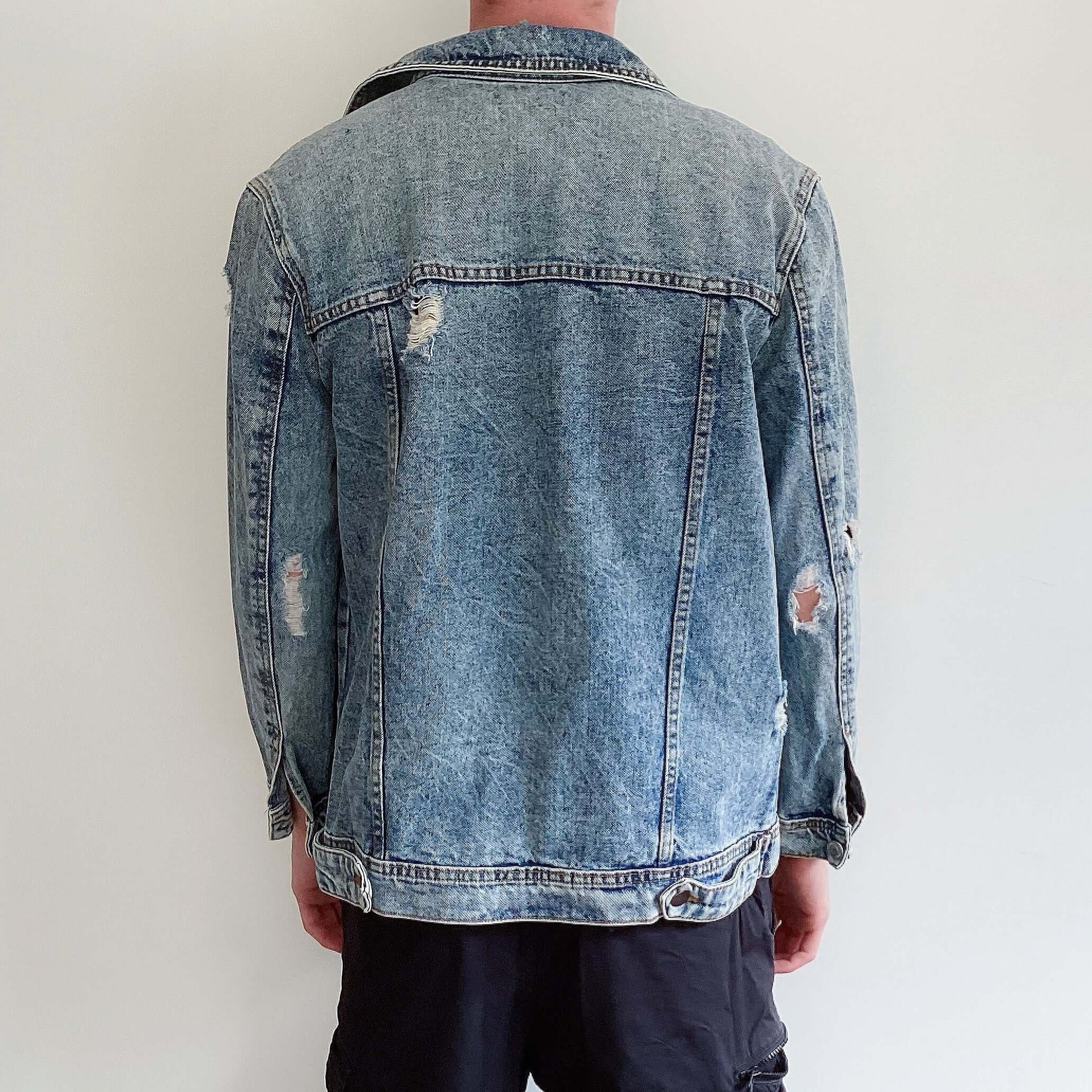 Blue snow-washed denim jacket with rips here and there shown from the back.