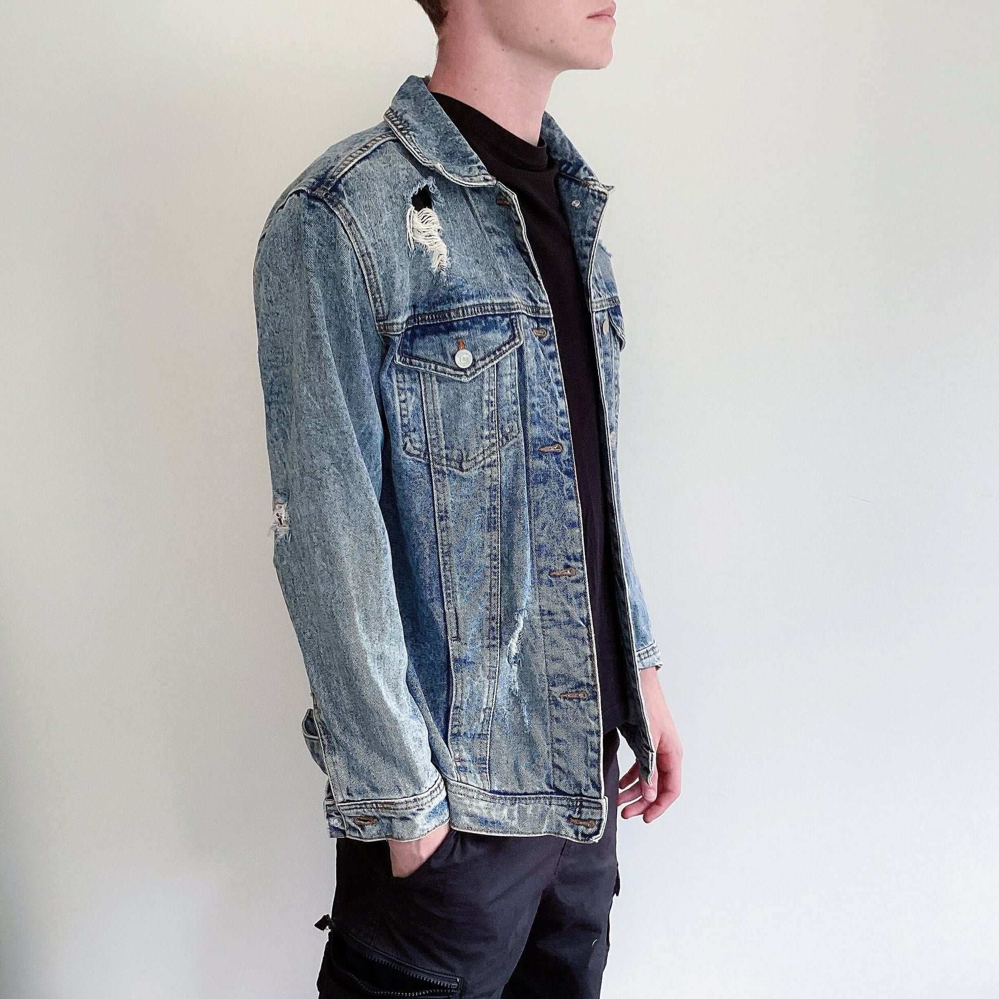 Blue snow-washed denim jacket with rips here and there side view.