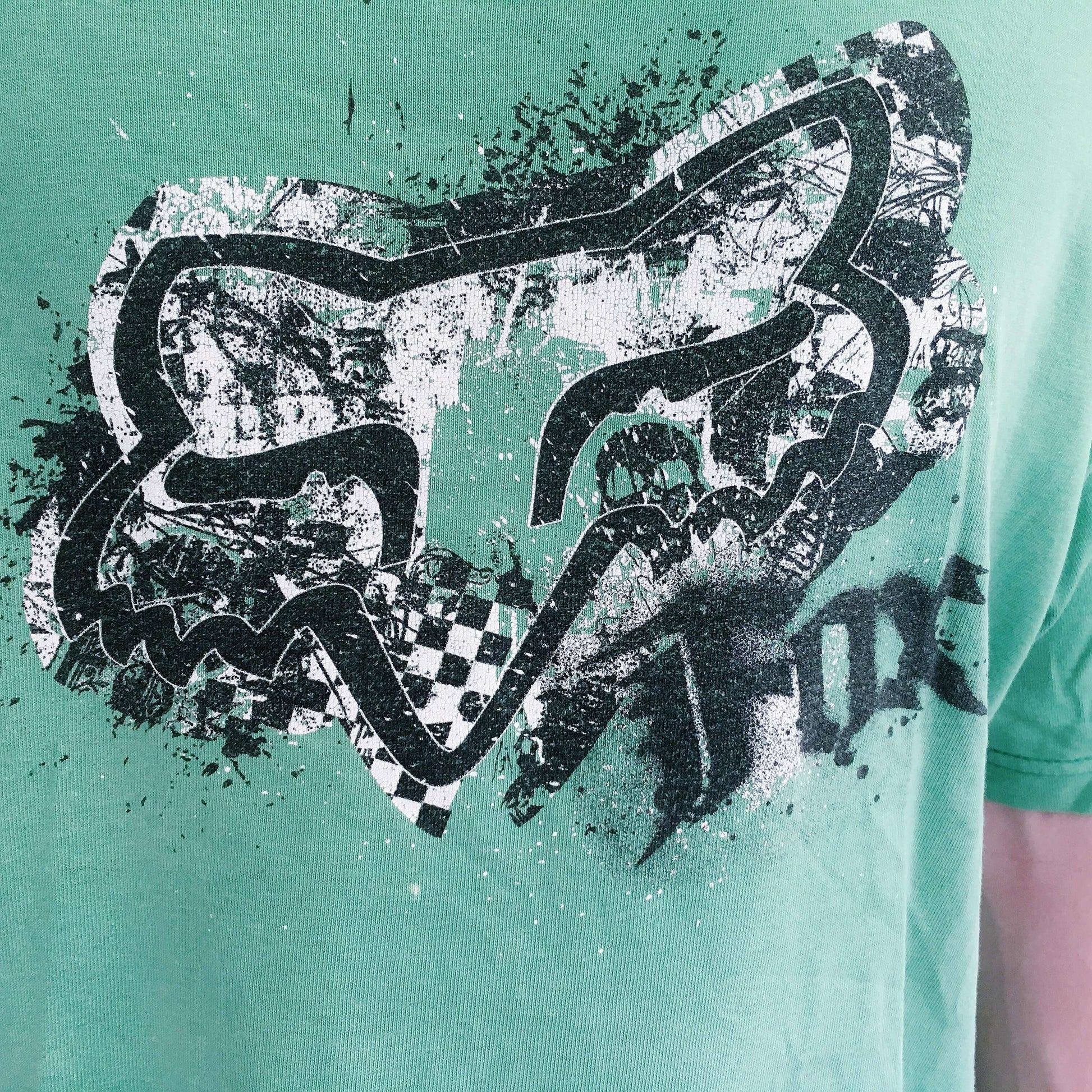 Detail view of aqua green drop shoulder tshirt, with black printing of the fox logo on the chest.