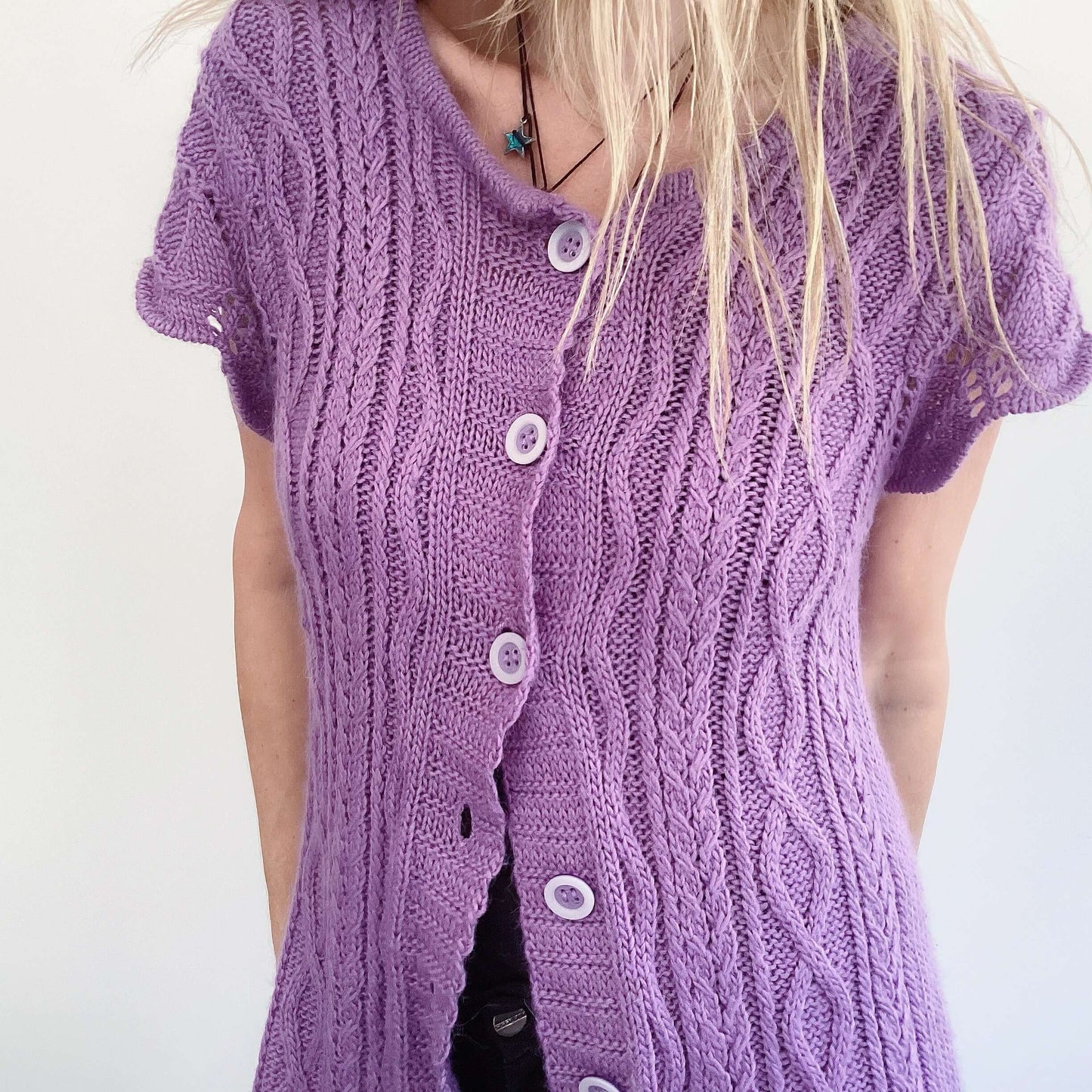 Front detail view of purple button up cardigan, celtic cable knit stitches, scalloped on the sleeves.