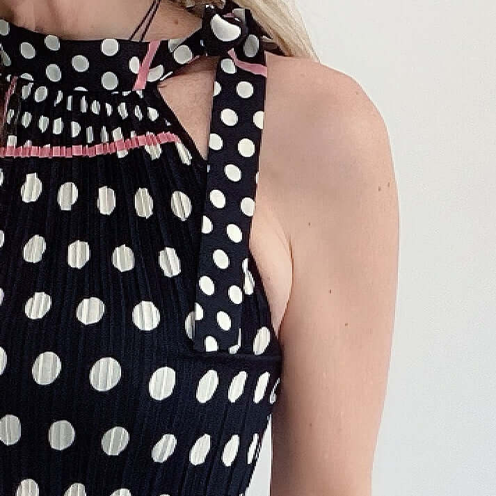 Detail view black and white polka dot top, pink piping accents, tied at the neck with matching fabric.