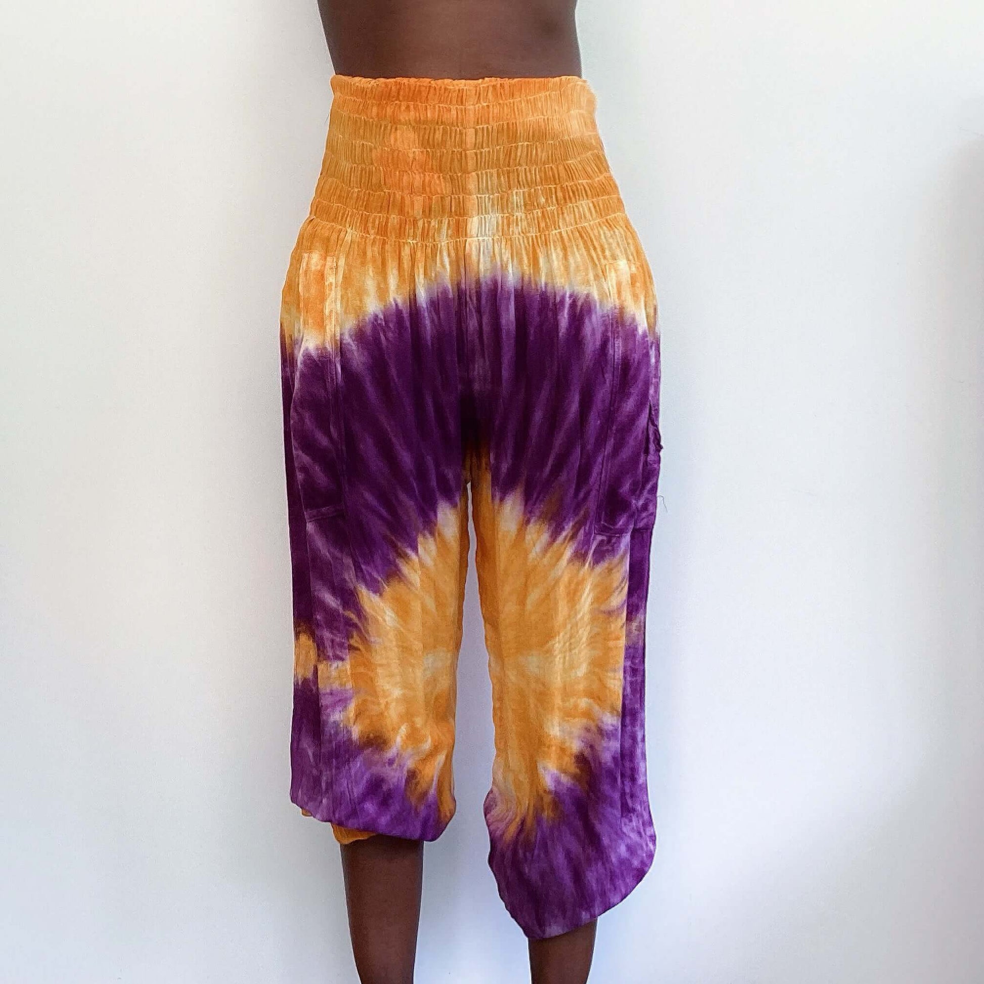 Front view of tie dyed orange and purple harem pants, ruched waistband, elasticated ankle.