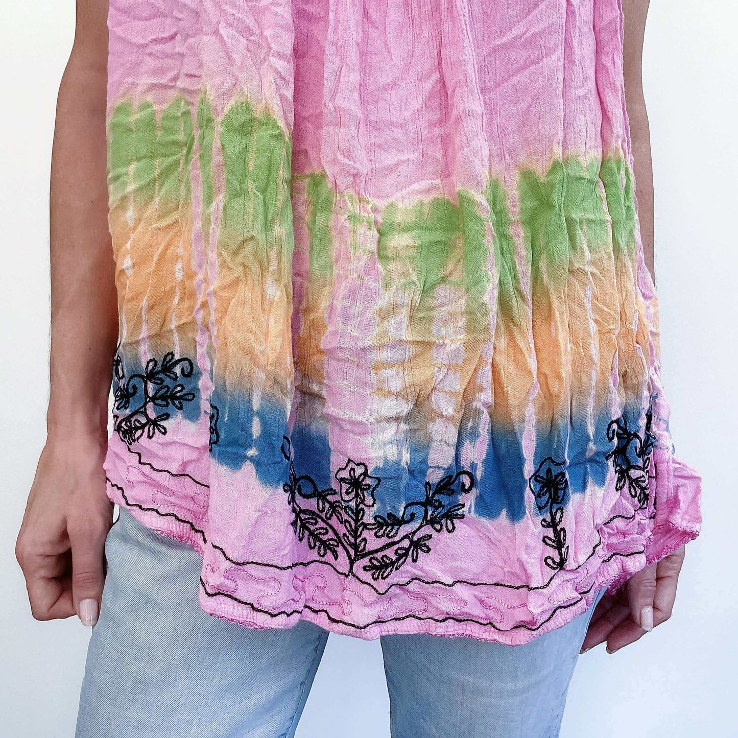 Detail view of tie-dyed pink top, embroidered edges, with blue, orange, green bands at the bottom.