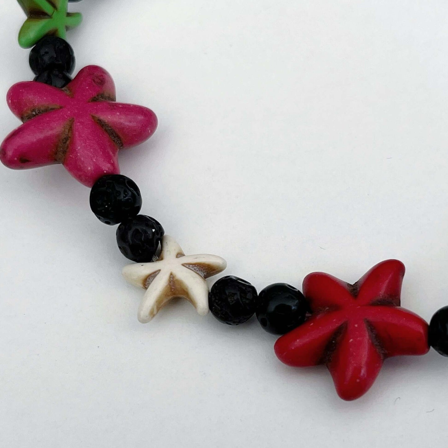 Detail view of anklet starfish, one large each of red and pink, one small each of green and white.