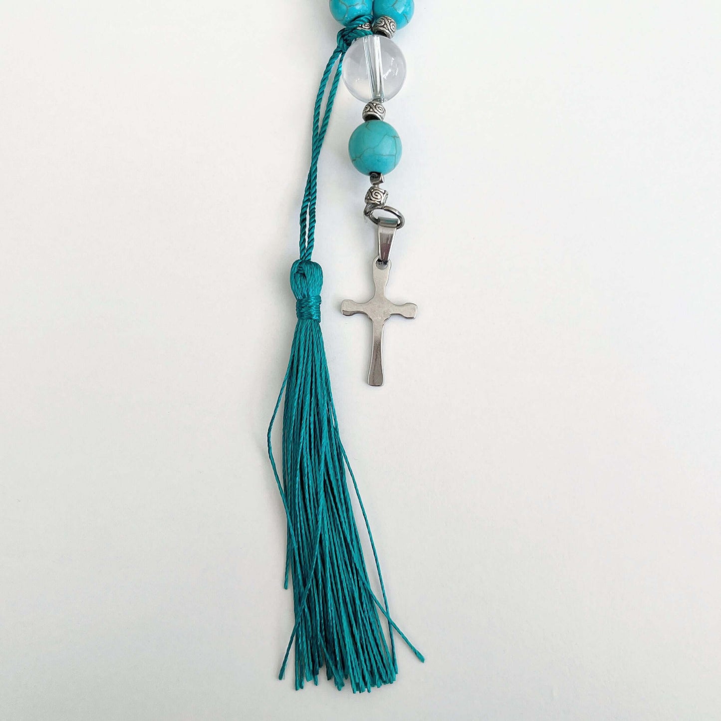 Detail view of prayer beads, Blue Howlite sections, with one clear quartz here and there. Cross and tassel at the bottom.