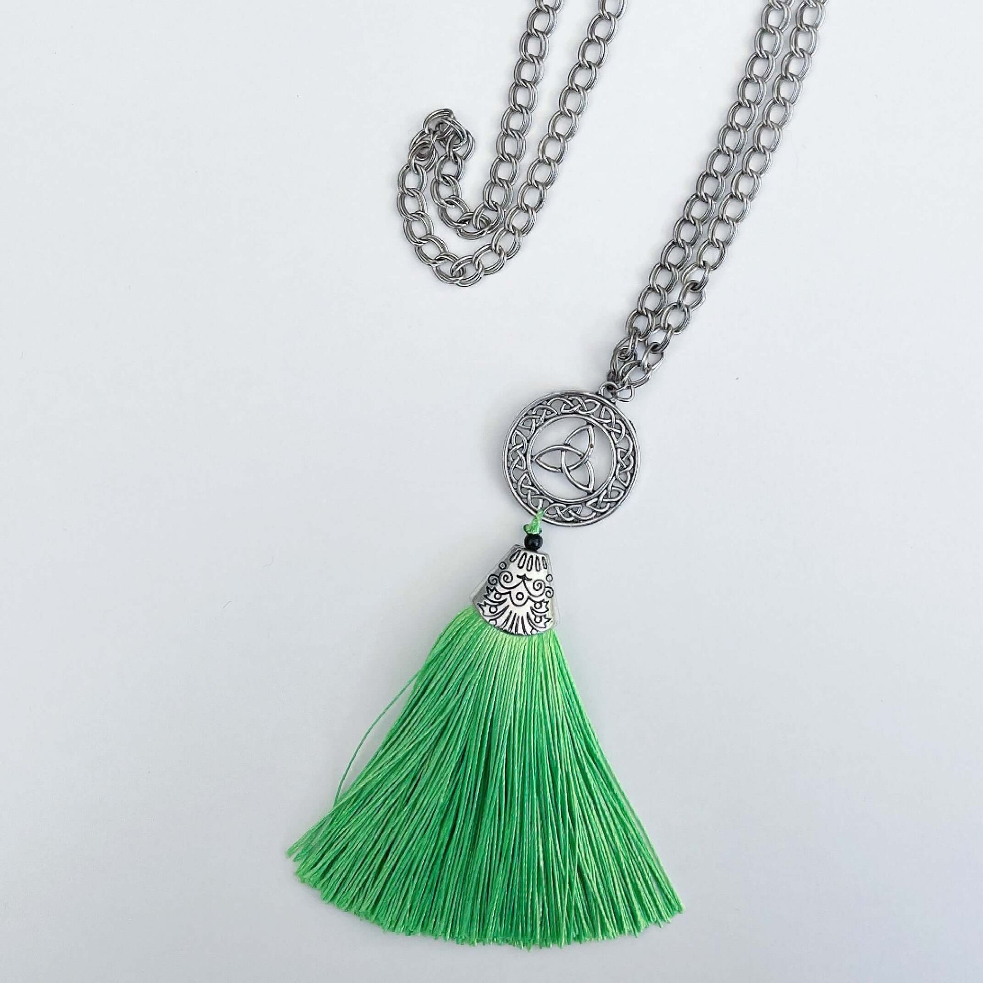 Top view of necklace with green tassel off the end, which has a silver finish filigree cap on it. Round link chain.