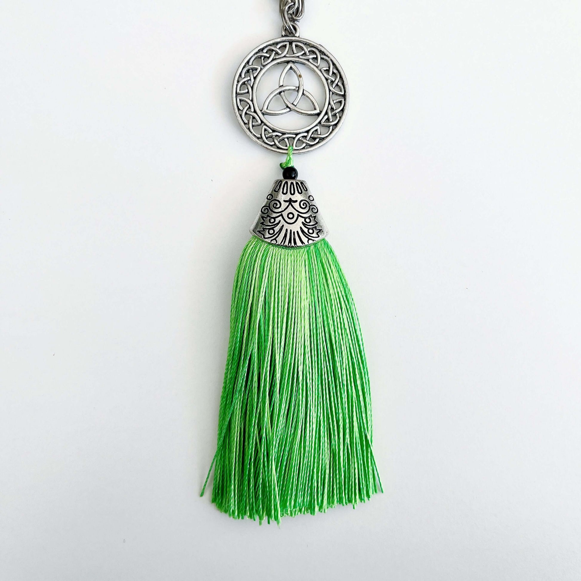 Detail view of necklace with green tassel off the end, which has a silver finish filigree cap on it.