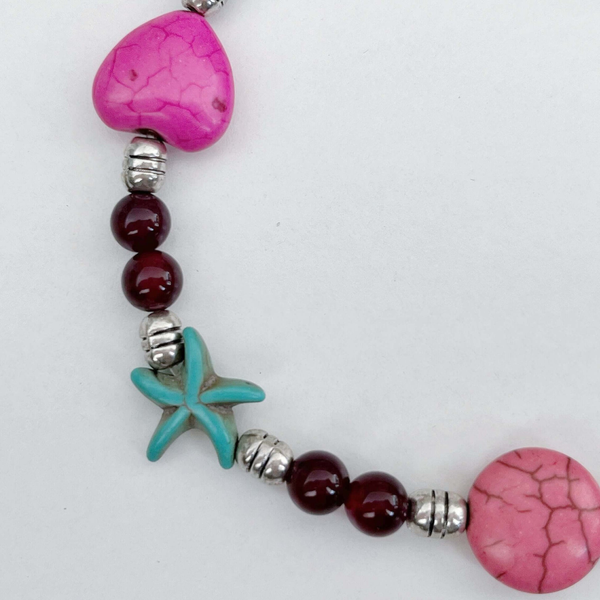 Detail view of anklet bead charms. Pink heart, turquoise starfish, orange starfish, pink smartie shape.