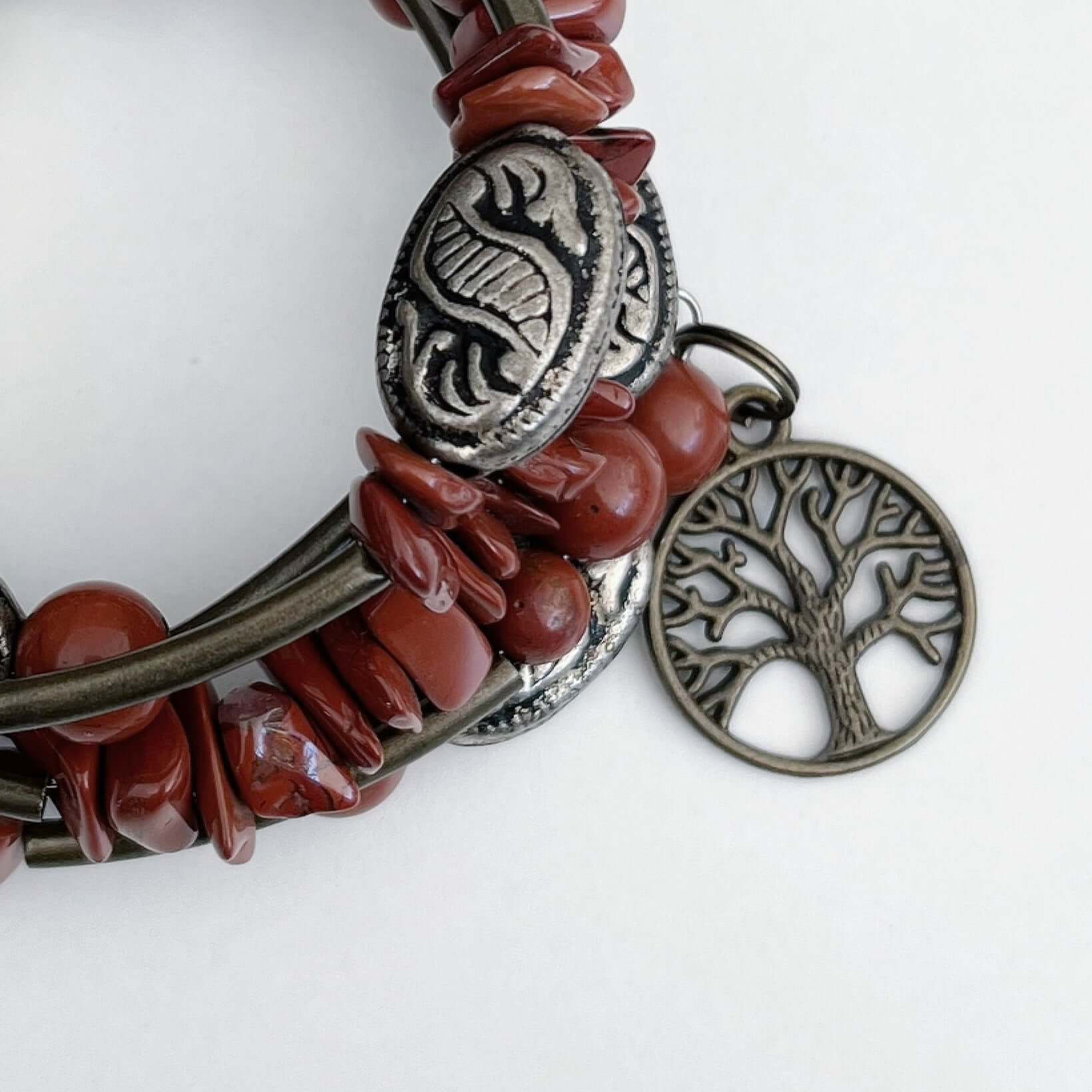 Detail of bracelet, both tumbled and round Red Jasper beads, showing bronze colored Tree Of Life on one end of the spiral.