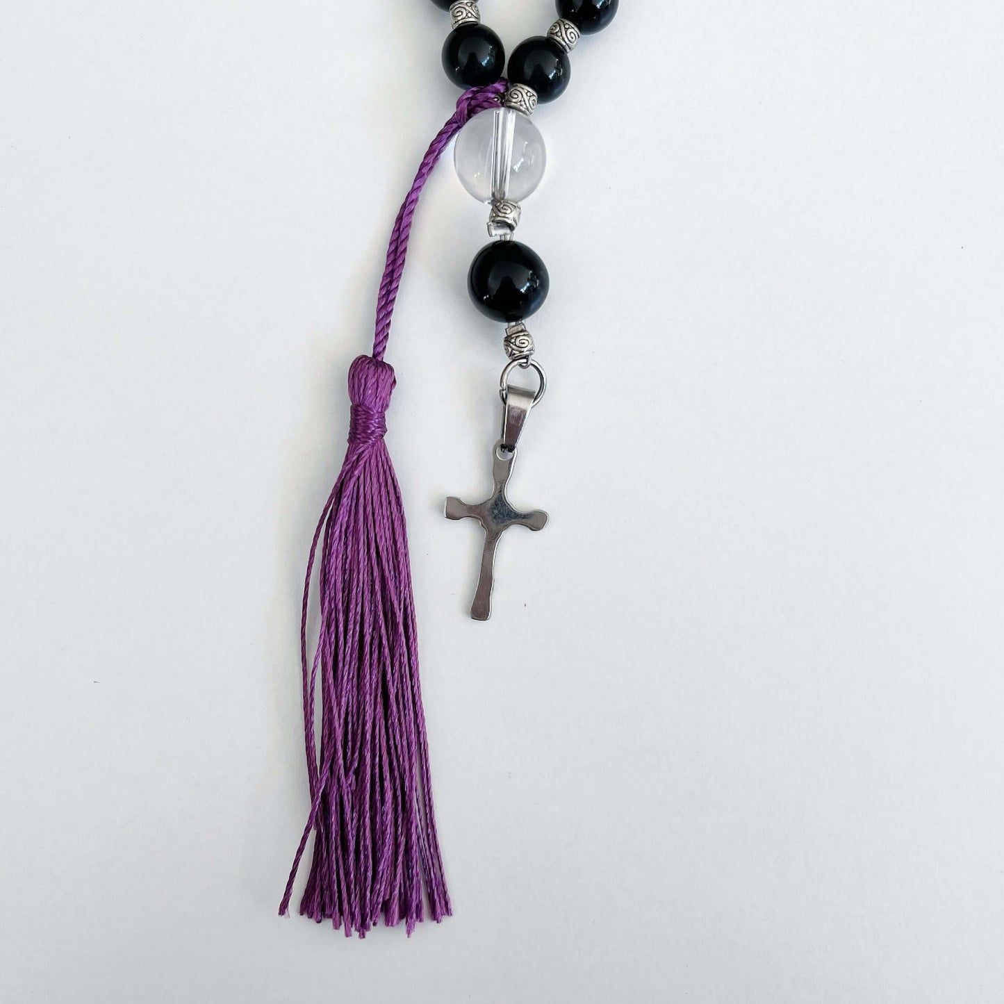 Detail view of prayer beads, Obsidian sections, with one clear quartz here and there. Cross and tassel at the bottom.