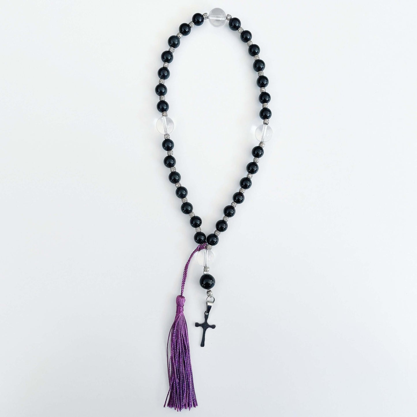 Top view of prayer beads, Obsidian sections, with one clear quartz here and there. Cross and tassel at the bottom.