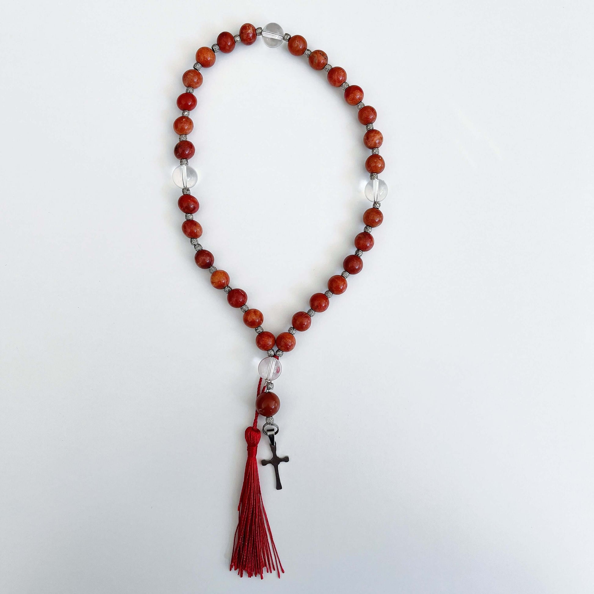 Top view of prayer beads, Coral sections, with one Clear Quartz here and there. Cross and tassel at the bottom.