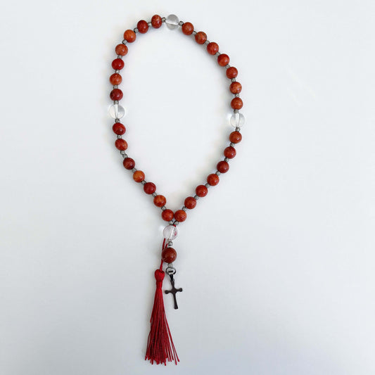 Top view of prayer beads, Coral sections, with one Clear Quartz here and there. Cross and tassel at the bottom.