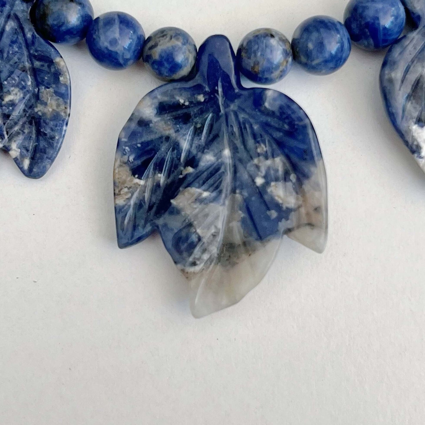 Detail view of necklace showing the central stone leaf, in striations of deep blue and off-white.