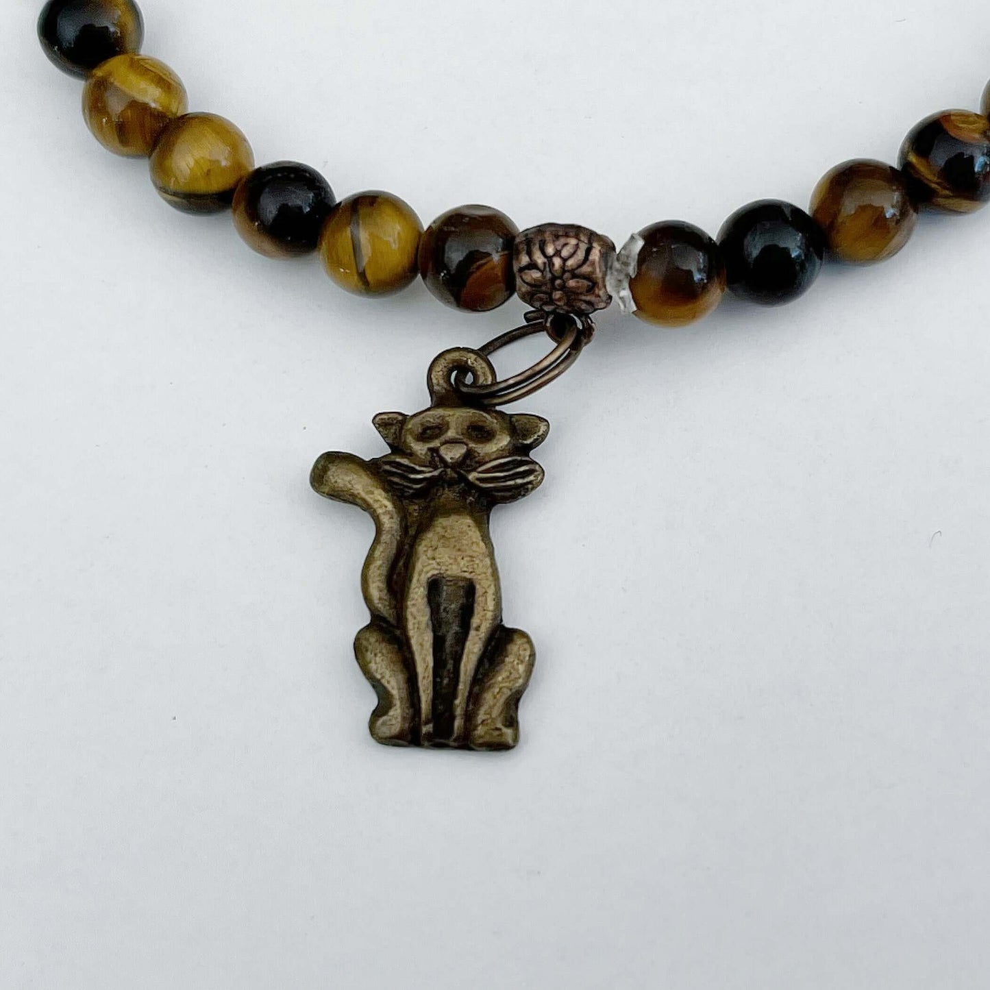 Detail view of the bronze colored cat sitting in upright position, tail up, with Tiger's Eye beaded either side.