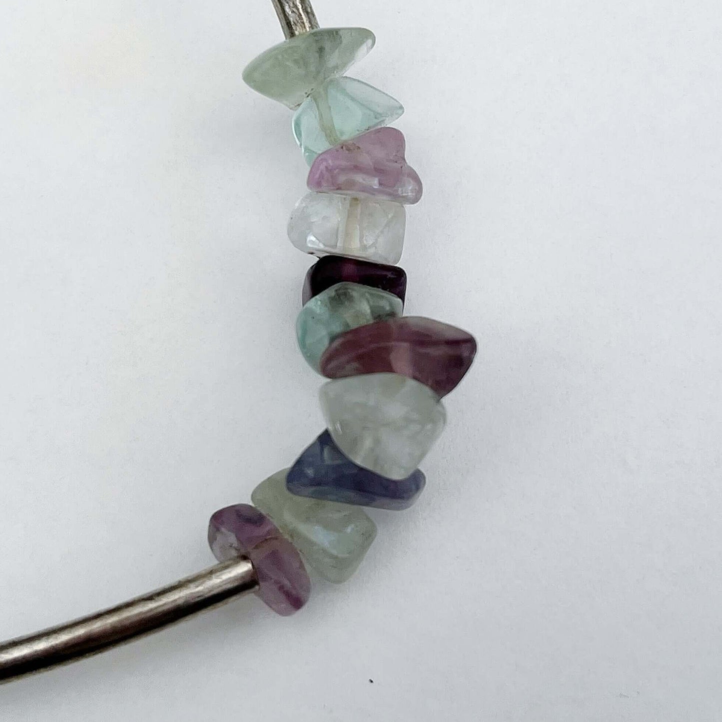 Detail view of the different stones chips, pale colors of purple, aquamarine, clear, with silver finish long tubular beads.