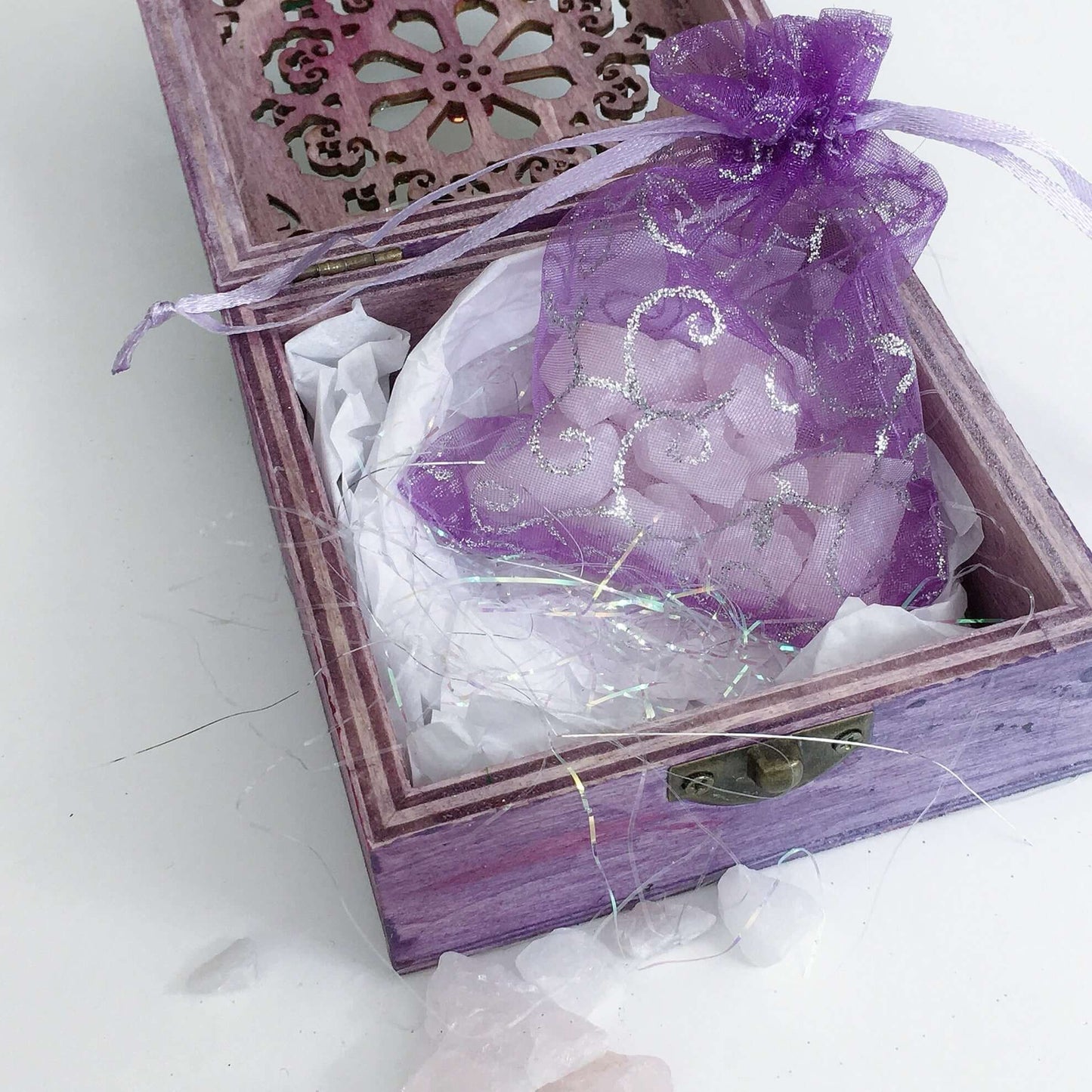 Close up view of rose quartz chips in purple organza pouch nestled in tissue paper and tinsel.