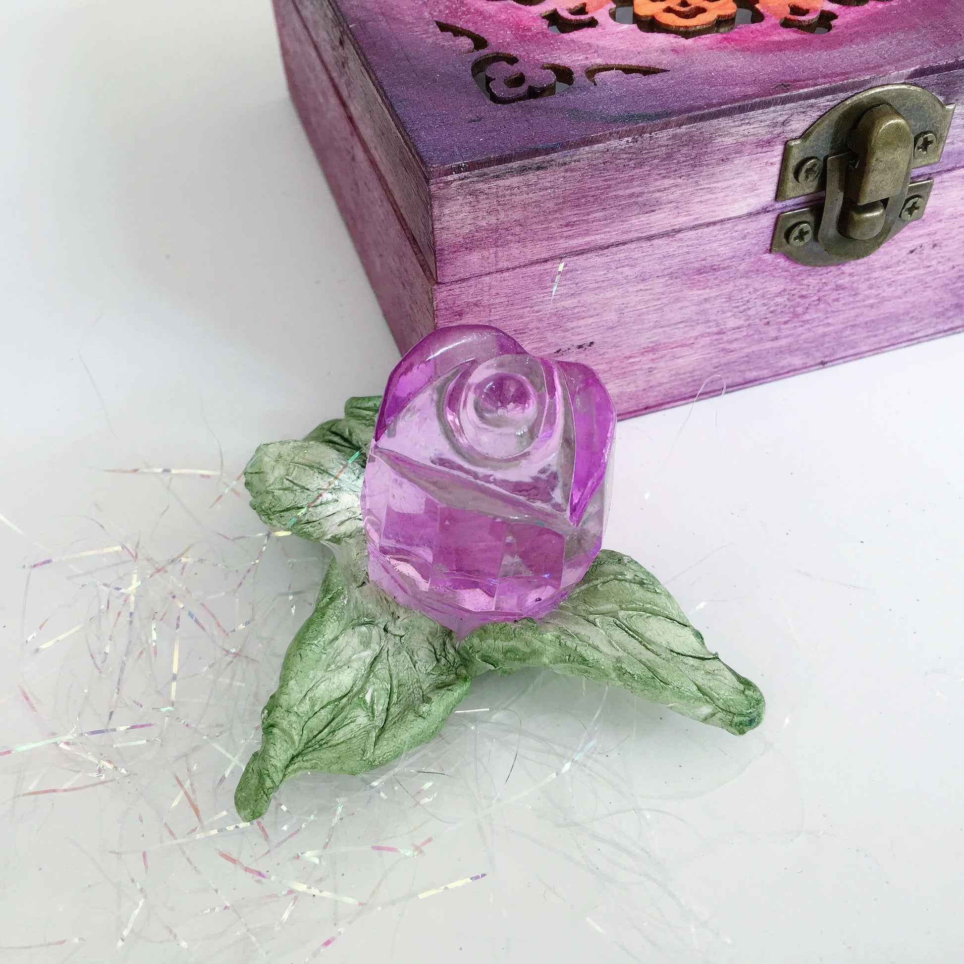 Detail view of purple glass rosebud and leaves, next to its box.