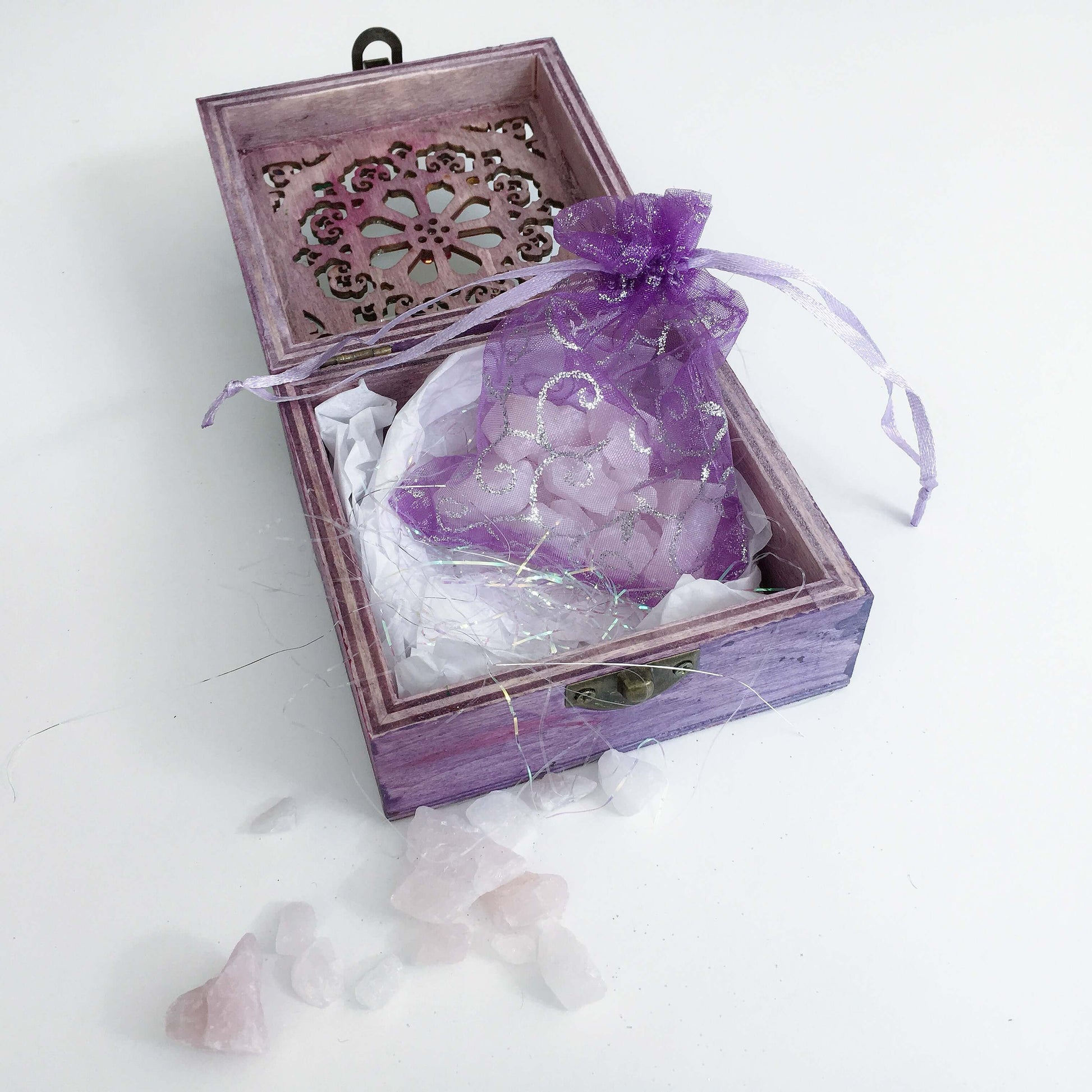 Contents detail view of rose quartz chips in purple organza pouch, nestled in tissue paper and tinsel.