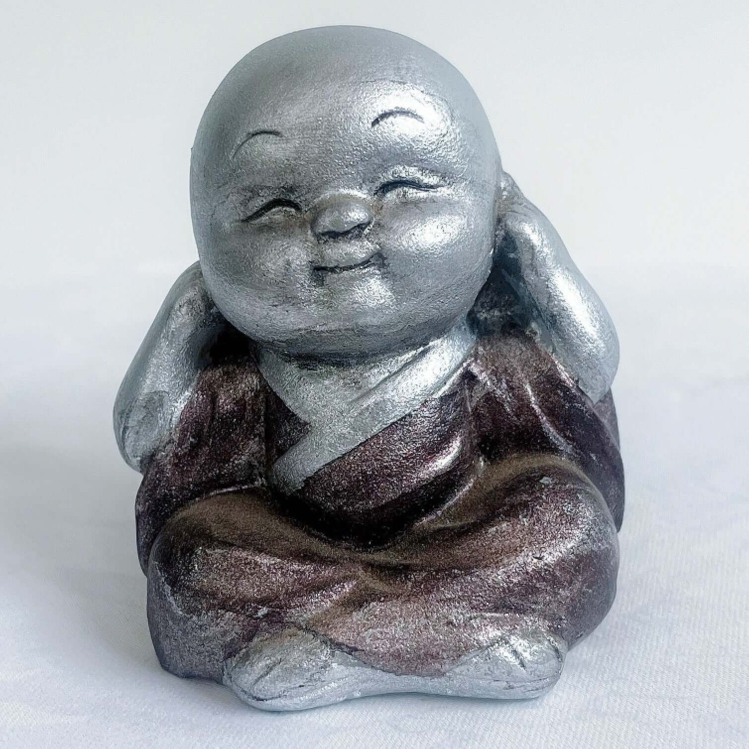 View of single monk, hear no evil, painted silver figure with bronze robes, and hands covering the ears.